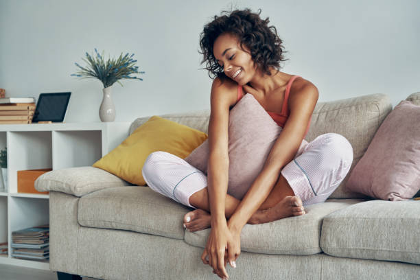 Beautiful young African woman smiling while relaxing on the couch at home stock photo