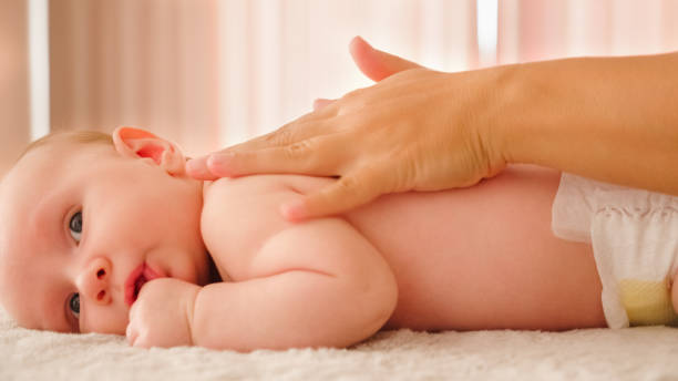 Mother doing massage on her healthy infant baby. Small caucasian newborn laying on his belly while his mother is performing a massage for his small back and developing muscles. stock photo