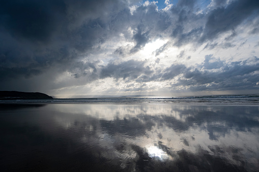A setting sun and dramatic skies over sea and beach in North Devon, Westward Ho!