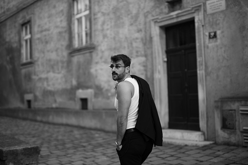 Fashionable dressed handsome young businessman walking in the street from work, holding his jacket and exploring the old city part. Black and white image