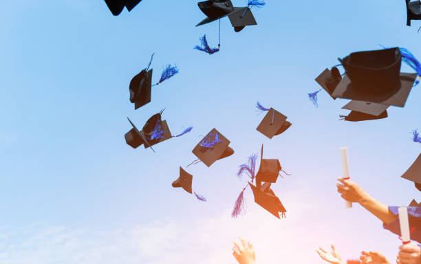 istock Graduating students hands throwing graduation caps in the air 1422515982
