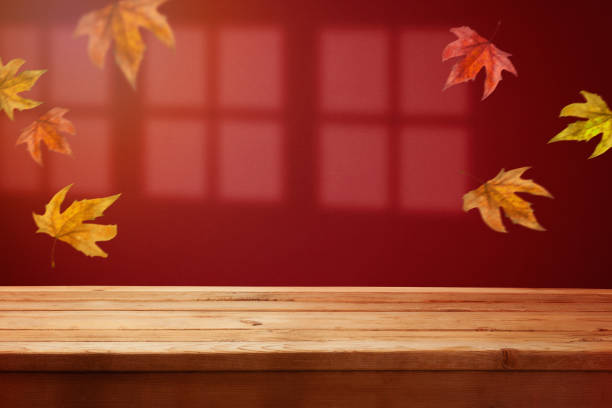 istock Empty wooden  table over trendy red wall background with window shadow and fall leaves.  Autumn season mock up for design and product display. 1422518348