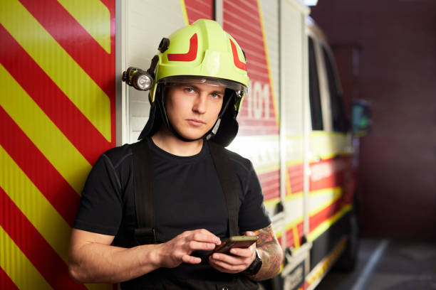 istock Portrait of a firefighter standing in front of a fire engine. Fireman using smart phone 1422520691