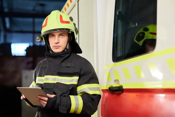 Photo of Male firefighter with tablet in uniform on car background