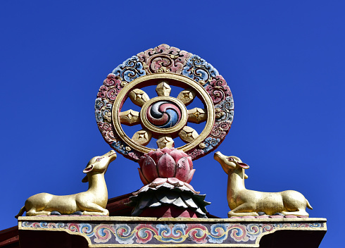 Zilukha, Thimphu, Bhutan: golden Dharma wheel on a lotus atop a pillar at Thangthong Dewachen Dupthop nunnery - the eight spokes represent the Noble Eightfold Path of Buddhism. Buddhists believe that the first turning of the wheel occurred when the Buddha taught the five ascetics at the Deer Park in Sarnath, because of this, dharmachakras are often represented with a deer on each side - Vajrayana Buddhism