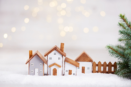 Happy New Year and Merry Christmas greeting card. Toy wooden houses, spruce branches on the background of a beautiful bokeh.