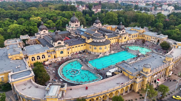 4K aerial drone view Szechenyi Bath. Drone flies around pool with many visitors after sunset. Budapest, Hungary