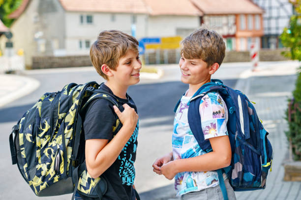 Two kid boys with backpack or satchel. Schoolkids on the way to school. Healthy smiling children, brothers and best friends outdoors on the street leaving home. Back to school. Happy siblings. stock photo