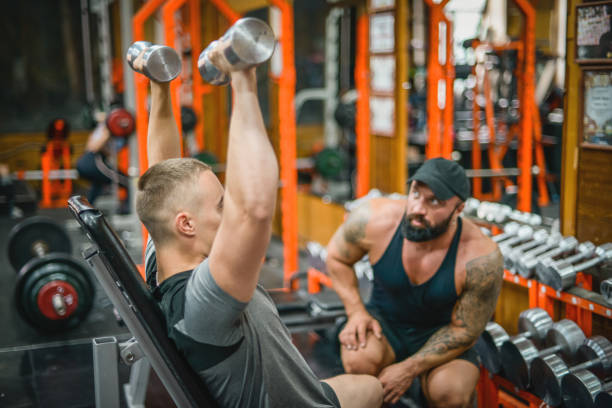 istock Man doing exercises in the gym with a man trainer athletic physique 1422532129