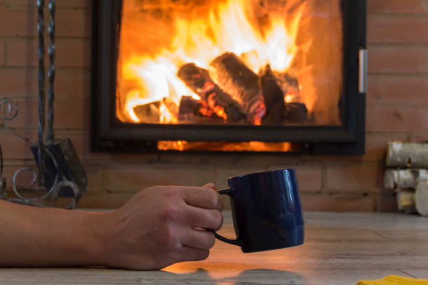 istock A man's hand holds a mug with a hot drink near the fireplace with a fire. Keep warm in a warm house in winter. 1422535530