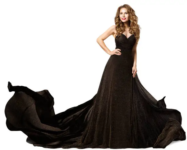Fashion Woman in Black Dress flying on Wind. Beauty Model with Curly Long Hair in Evening Gown. Elegant Lady dancing in Luxury Dress happy smiling over White isolated