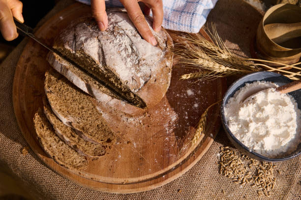 istock Overhead view of a baker slicing whole grain bread on a cutting board with a kitchen knife. 1422552557