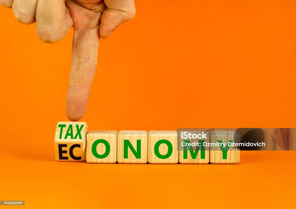 Taxonomy or economy symbol. Businessman turns wooden cubes and changes the concept word Economy to Taxonomy. Beautiful orange background. Business ecology taxonomy or economy concept. Copy space. Education Stock Photo