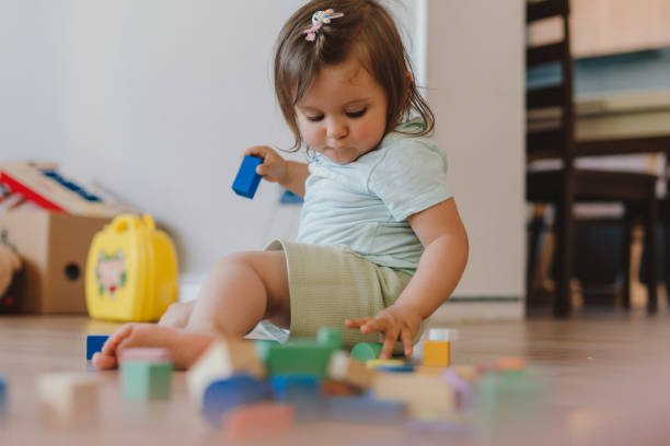 Focused baby girl sitting on the floor building something of multi-colored blocks of the constructor. Smiling happy child. Baby development. Focused baby girl sitting on the floor building something of multi-colored blocks of the constructor. Smiling happy child. Baby development. motor skills in babies stock pictures, royalty-free photos & images