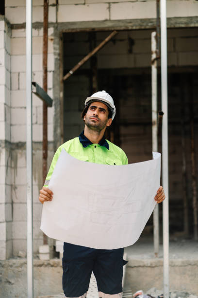 istock Construction worker in hardhat and vest looking up and holding  blueprint on construction site 1422556993