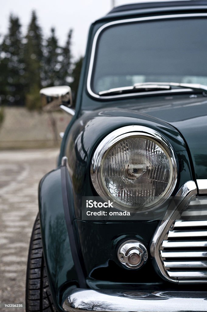 Front of a dark green mini cooper with one headlight shown Particular of vintage classic english car in green color front View Car Stock Photo