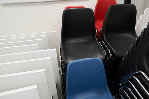 Black and blue plastic chairs are stacked next to folded iron stands. A lot of plastic chairs stand on top of each other against the background of the wall. High quality photo