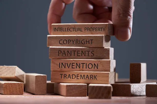 Photo of man adding a  block showing the words Intellectual property on top of  other wooden block with text copyright, patents,  invention,and trademark