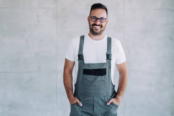 istock Young male worker in an overall uniform posing at his workplace. 1422565468
