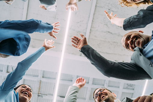 Shot of group of business people celebrating their success in the office. Multiracial group of corporate business persons on a business meeting in modern office. Cheerful business team raising their hands together in the air.