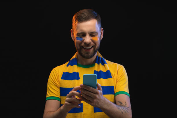 студийный портрет улыбающегося счастливого футбольного болельщика, делающего ставки на любимую команду на сайте букмекерской конторы с п� - американский футбольный игрок стоковые фото и изображения