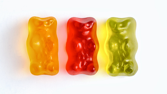 Three brightly colored gummy bears in front of a white background