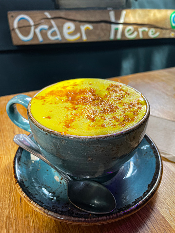 Stock photo showing close-up view of blue cup and saucer of turmeric latte coffee served on a wooden cafe table.