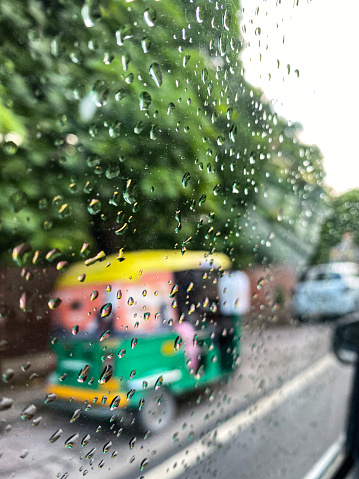 New Delhi, India - August 16, 2022: Stock photo showing dangerous driving with overloaded auto rickshaws transporting passengers in New Delhi, India as viewed through a car window covered in raindrops and condensation.