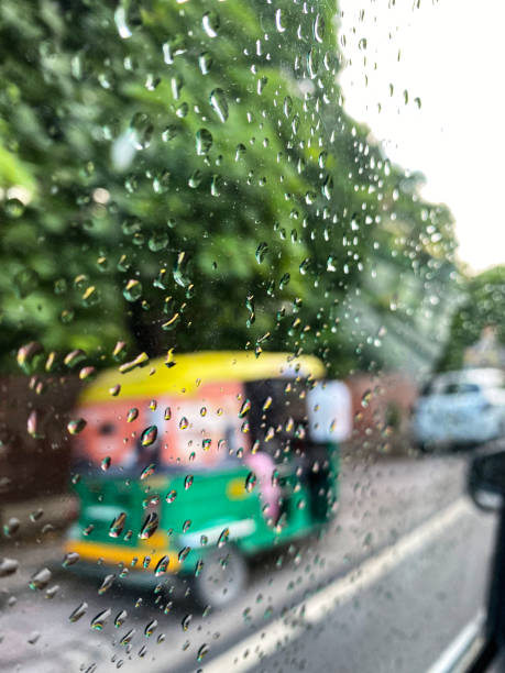 image of indian auto rickshaw taxi cabs travelling on highway, yellow and green tuk tuk transporting too many passengers, dangerous driving viewed through raindrops on car window, driving in wet weather, new delhi, india - consumerism indian ethnicity india delhi imagens e fotografias de stock