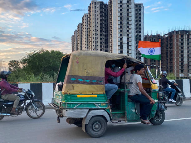 image of indian auto rickshaw taxi cab flying national flag of india (tricolour) and motorbikes travelling on highway, yellow and green tuk tuk transporting too many passengers, people riding motorcycles, dangerous driving around new delhi, india - consumerism indian ethnicity india delhi imagens e fotografias de stock