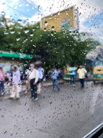 New Delhi, India - August 16, 2022: Stock photo showing Indian traffic and pedestrians viewed through a car window covered in raindrops and condensation, on a rainy day in New Delhi, India.