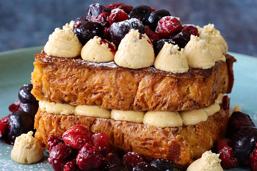 Stock photo showing close-up view of eggy brioche bread sandwich with Chantilly cream, blackcurrants and cherries.
