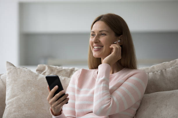 wesoła kobieta użytkownika smartfona dotykająca bezprzewodowych słuchawek w uchu - cotton swab audio zdjęcia i obrazy z banku zdjęć