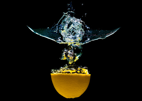 Halved citrus fruit dropped in water with splashes isolated on black background.