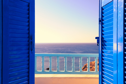 Blue Shutters Open onto Sea and Sky at Dawn with sunlight brightly striking the shutter on the right