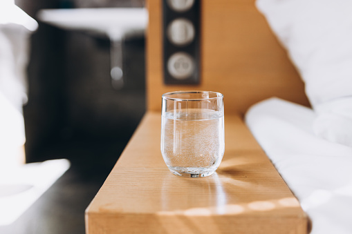 Glass of water on wooden table bokeh background. Good habit - drinking a glass of water before going to sleep.