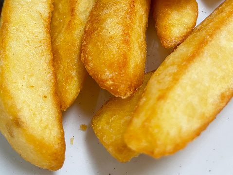 Stock photo showing close-up, elevated view of white plate containing a pile of golden brown, freshly cooked chipped potatoes.