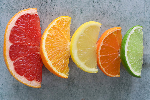 Stock photo showing close-up, elevated view of a row of citrus fruit slice wedges against a mottled grey background.