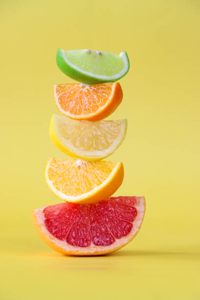 imagen en primer plano de rodajas de cuña alternas de pila de cítricos, rodajas de lima, naranja, limón y pomelo rosa, fondo amarillo, enfoque en primer plano - fruta cítrica fotografías e imágenes de stock