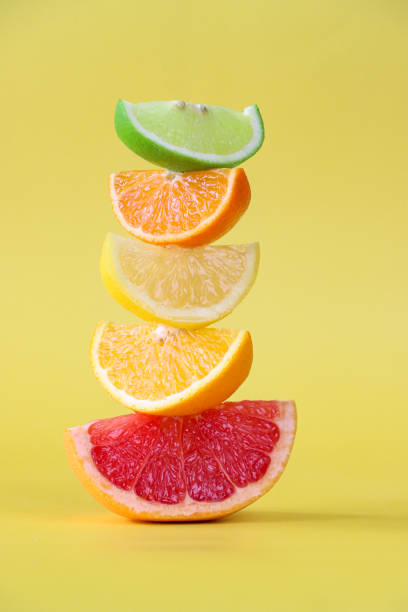 Close-up image of alternating wedge slices of citrus fruit pile, lime, orange, lemon and pink grapefruit wedges, yellow background, focus on foreground stock photo