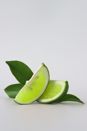 Stock photo showing citrus fruit wedges on white background, modern minimalist photo of sliced lime citrus fruit showing seeds / pips and rind around edge, healthy eating concept photo for vitamin C and fruit juice.