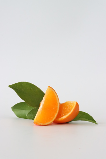 Stock photo showing citrus fruit wedges on white background, modern minimalist photo of sliced satsuma citrus fruit showing seeds / pips and rind around edge, healthy eating concept photo for vitamin C and fruit juice.