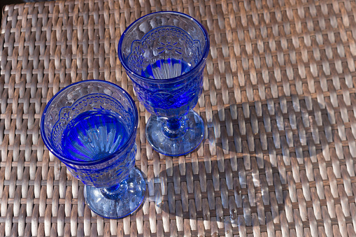 Two blue glass glasses with water are on a table made of artificial rattan. A sunny summer day.