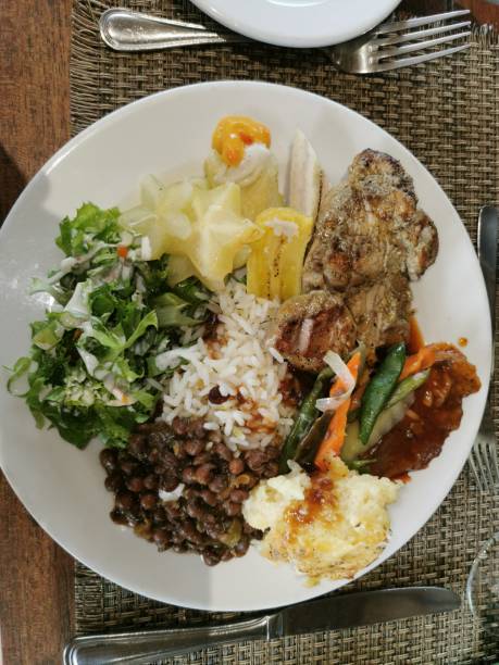 A lunch meal made of rice, stewed pigeon peas, grilled fish, steamed vegetables, green salad, five finger or carambola salad, boiled plantain, breadfruit pie and other boiled provisions- yam, dasheen, cassava.