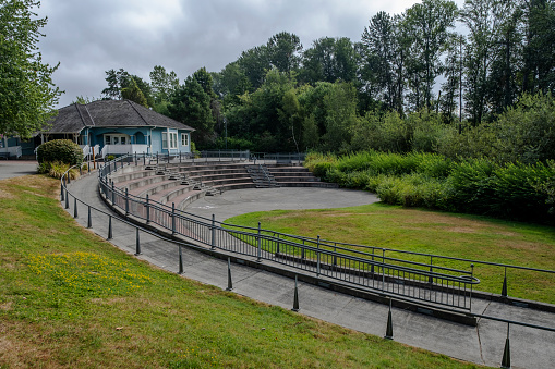 An outdoor amphitheater and a building are shown in a public park in a small American town. Sky is filled with clouds.
