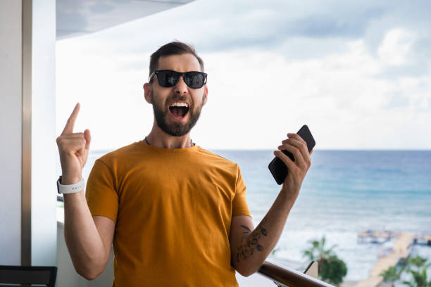 un eufórico fanático del fútbol está viendo jugar al fútbol en vivo en línea en su teléfono móvil, apostando en su equipo favorito y celebrando la ganancia de dinero - suit soccer men sport fotografías e imágenes de stock