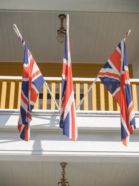 Three Union Jack flags on poles on exterior of colonial style building
