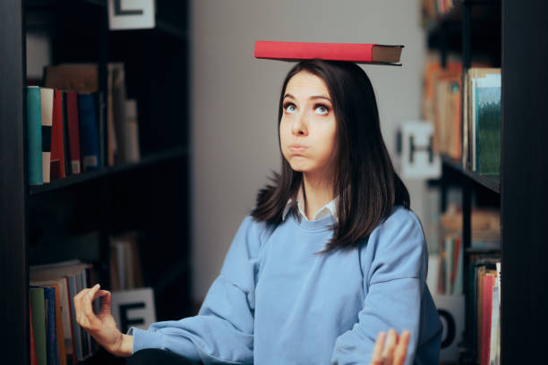 Studious Woman Balancing a Book on her Head Sitting in a Library stock photo