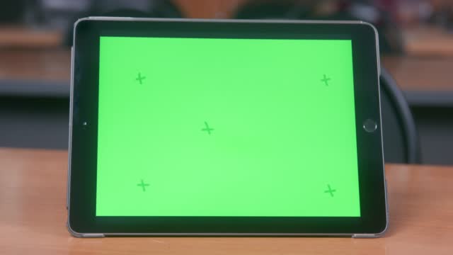 Digital tablet in case is on table, chromakey on display, front view.