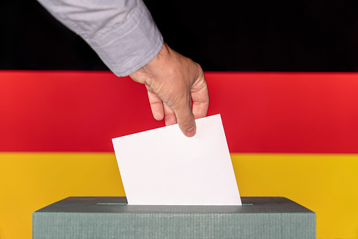 Man putting a ballot into a voting box against the background of the Germany flag